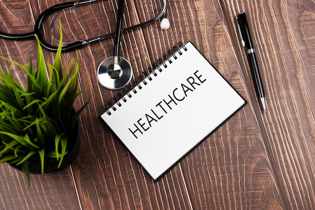 Healthcare text on note pad with stethoscope pen and green potted plant Health and medicine concept