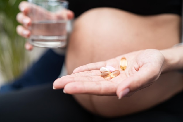 Healthcare treatment supplements young pregnant woman holding pills and glass of water in her hand b