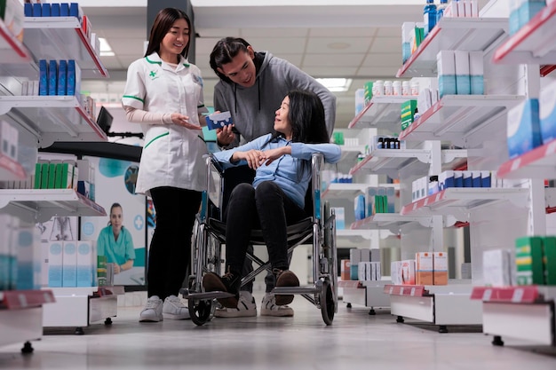 Healthcare worker giving pills box to woman and young man, client dealing with chronic disability in pharmacy shop. Asian customers asking pharmacist to help with medicinal supplements.