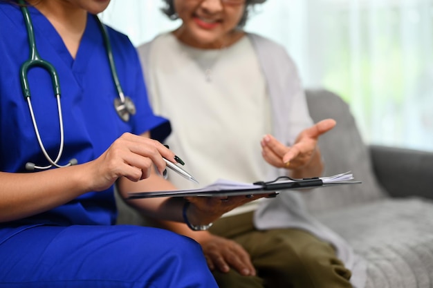 Медицинский работник указывает на планшет, показывающий результаты анализов здоровья пожилому пациенту во время домашнего визита