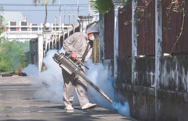 古いフェンスの壁近くの排水溝で蚊を駆除するために化学薬品を散布する医療従事者