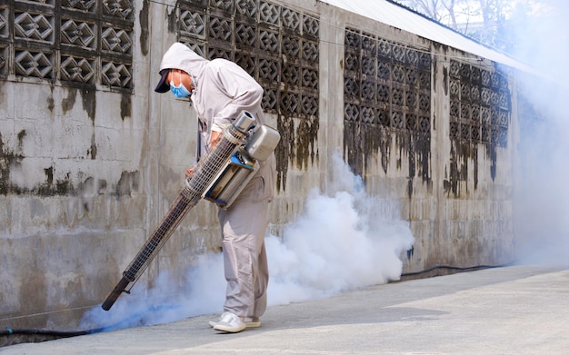 Healthcare worker spraying insecticide in drainage ditch near fence wall in residential community