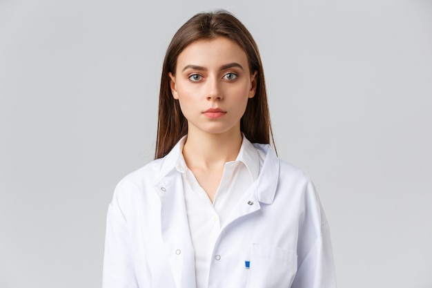 Healthcare workers, medicine, insurance and covid-19 pandemic concept. Young professional physician or doctor in white scrubs, looking serious at camera, working in hospital or clinic with patients