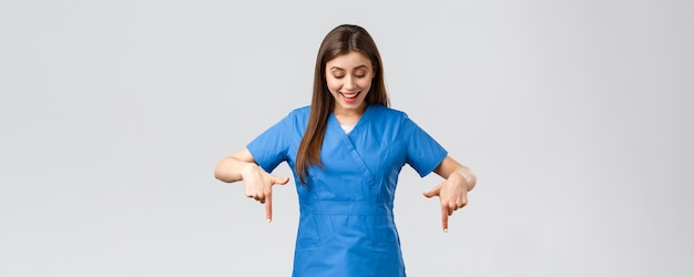 의료 종사자들은 바이러스 covid19 테스트 스크리닝 의학 개념을 예방합니다. 행복하고 흥분한 예쁜 여성 간호사 또는 파란색 수술복을 입은 의사가 손가락을 아래로 가리키는 좋은 소식을 읽으면서 웃고 있습니다
