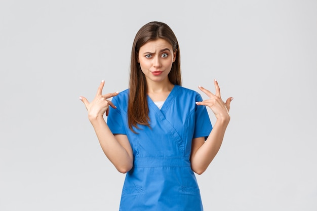 Healthcare workers, prevent virus, insurance and medicine concept. Funny displeased female nurse in blue scrubs grimacing, freak out over something, mimicking and staring camera shocked