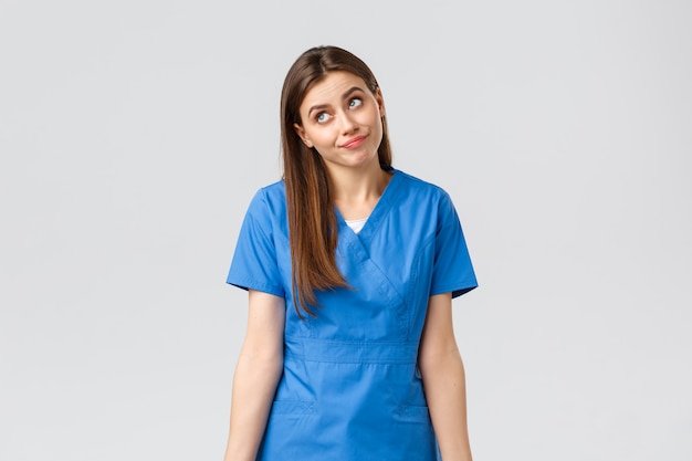 Healthcare workers, prevent virus, insurance and medicine concept. Indecisive and unsure cute doctor, female nurse in blue scrubs, cant tell, have no idea, shrugging and look away uncertain