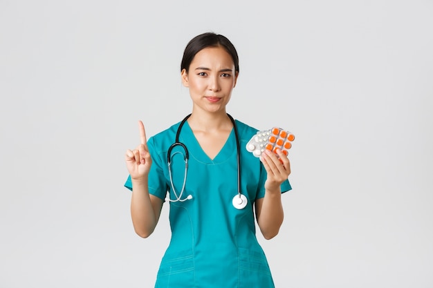 Healthcare workers, preventing virus, quarantine campaign concept. Reluctant and disappointed asian female physician, doctor shaking finger in disapproval, scolding patient for taking medication