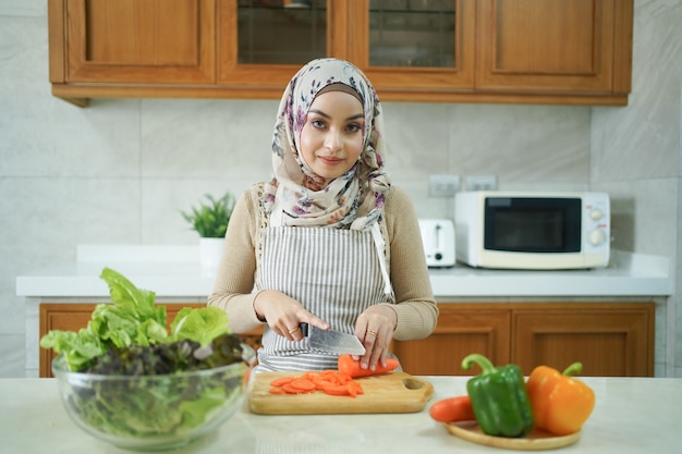 健康なアジアのイスラム教徒の女性は、キッチンで調理する野菜を準備しています