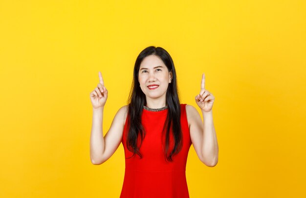 Healthy Asian woman adult wearing beautiful sleeveless dress pointing fingers to high above on bright yellow background.