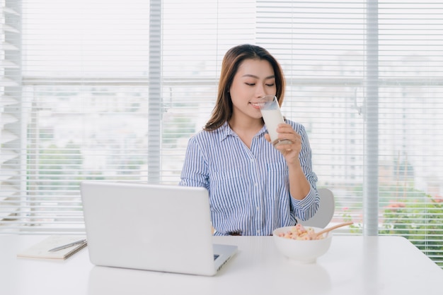 Healthy asian woman drinking a glass of milk at desk in office