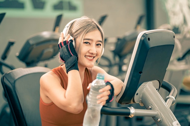 フィットネスジムで運動しながらヘッドフォンで音楽を聴く健康なアジアの女性