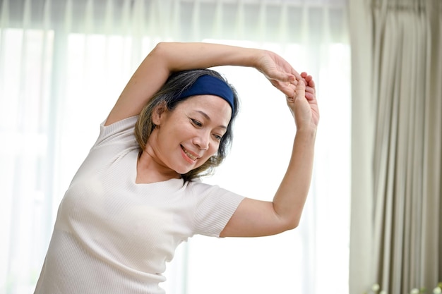 Healthy Asianaged woman exercising at home practicing yoga stretching her arms