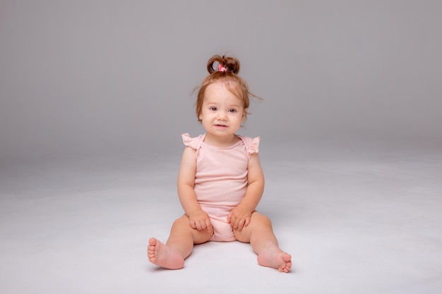 분홍색 바디슈트를 입은 건강한 아기 소녀는 텍스트를 위한 흰색 배경 공간에 앉아 있습니다.