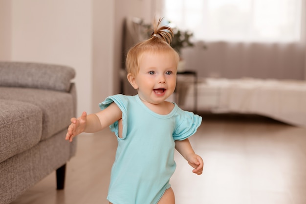 healthy baby girl in a room next to a gray sofa is learning to walk