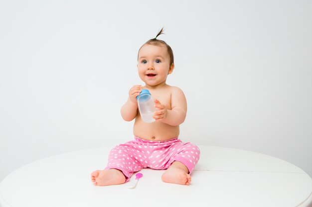 Healthy baby girl smiles and holds a water bottle