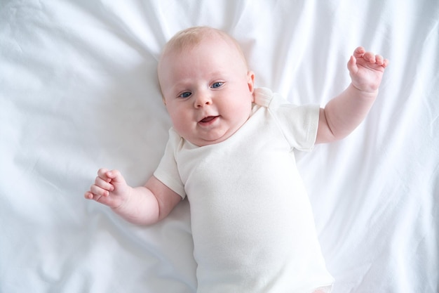 Photo healthy baby lies on his back on bed on white bedding top view