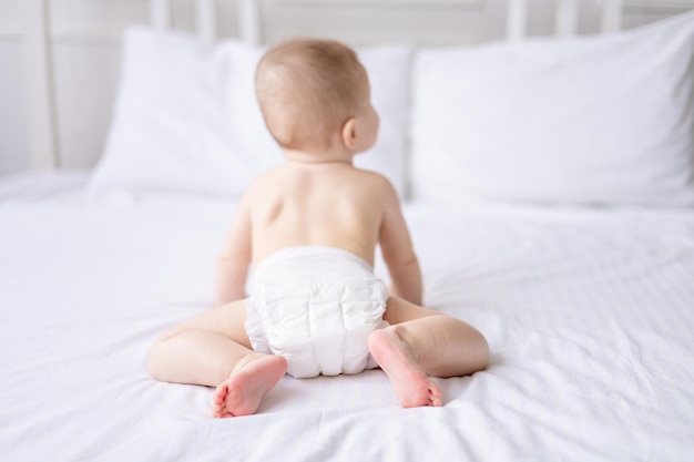 Photo a healthy baby naked in panties crawls on the bed on white bedding the child turned his back