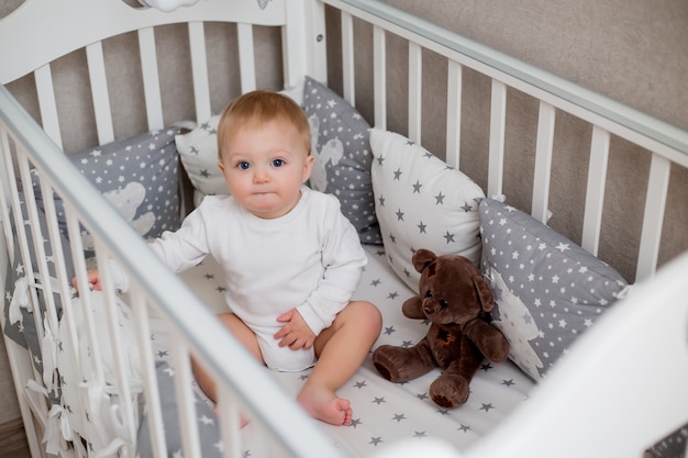 healthy baby in white clothes is sitting in a child's bed