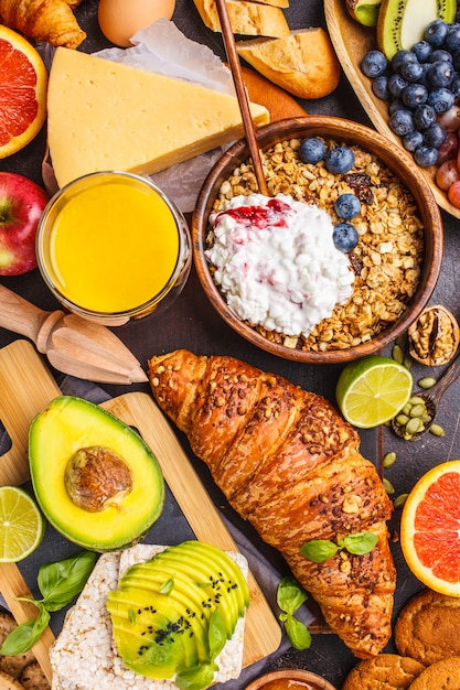 Healthy balanced breakfast on a dark background. Muesli, milk, juice, croissants, cheese, biscuits.