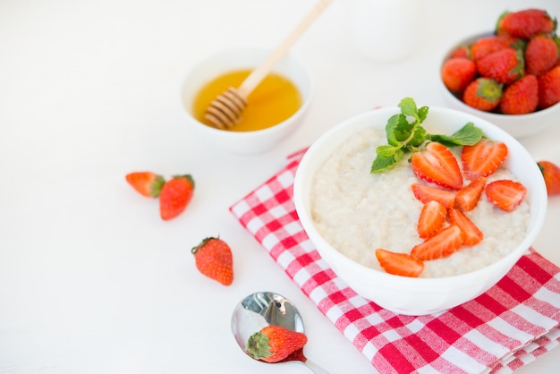 Healthy balanced Breakfast of oatmeal with strawberries and honey on a white wall. Horizontal photo with copy space.