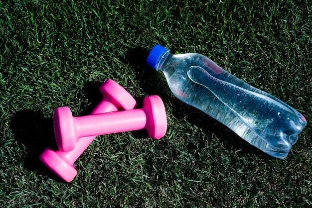 Foto uno stile di vita sano ed equilibrato mantiene l'equilibrio idrico nel corpo mentre si allenano bilancieri e bottiglia su erba verde attrezzi sportivi e attrezzature manubri nel parco idratazione dopo il fitness