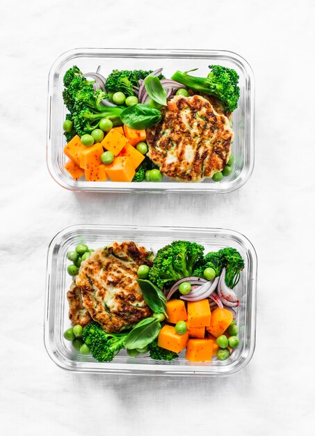 Healthy balanced lunch box Grilled chicken zucchini burgers with broccoli pumpkin green pea salad on a light background