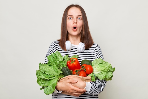 Photo healthy beating useful food astonished surprised woman embraces fresh vegetables looking at camera with open mouth posing isolated over white background