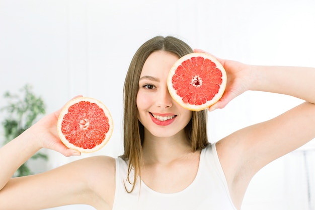 Healthy, beautiful smile, cute happy girl holding halves of grapefruit near face. Healthy food concept.  Vitamins and minerals.