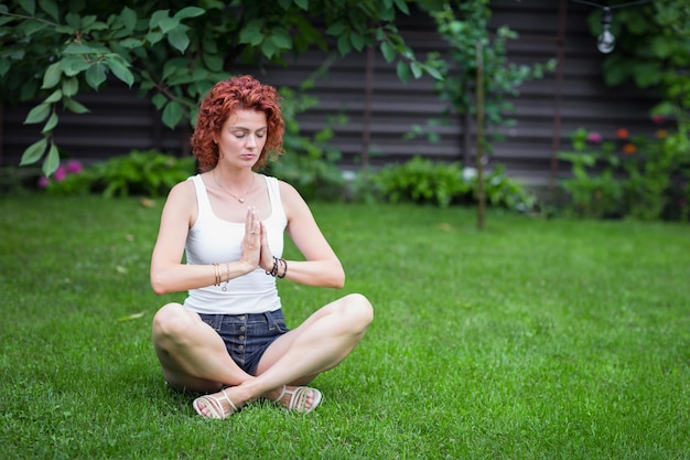 Healthy beautiful woman practicing yoga outdoor in back yard sitting in lotus pose on grass meditating smiling relaxed with closed eyes Mindfulness meditation well being concept