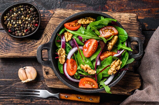 Healthy bistro green salad with mix leaves mangold, swiss chard, spinach, arugula and nuts in a pan. Dark wooden background. Top view.