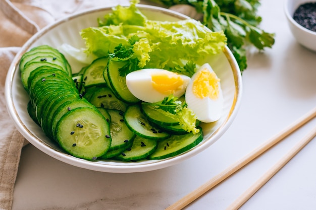 Healthy bowl, cucumber salad with eggs and coriander on marble background