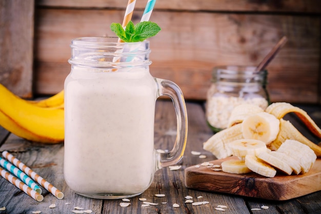 Healthy breakfast banana smoothie with oat flakes in glass mason jar on a wooden background