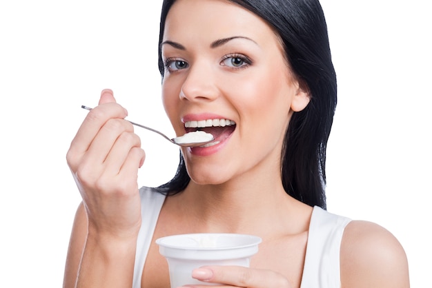健康的な朝食。白い背景に立っている間サワークリームとスプーンを保持している美しい若い笑顔の女性