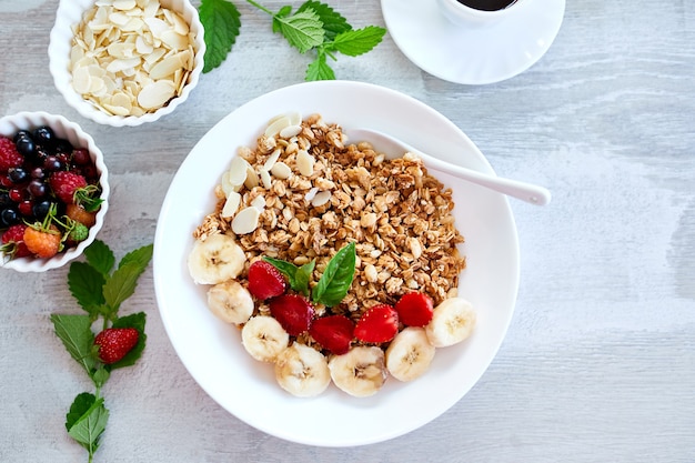 Healthy breakfast bowl, fresh granola, muesli with yogurt fruits and coffee, strawberry, banana on white table, Top view, Copy space. Clean eating, detox, dieting, vegetarian food concept