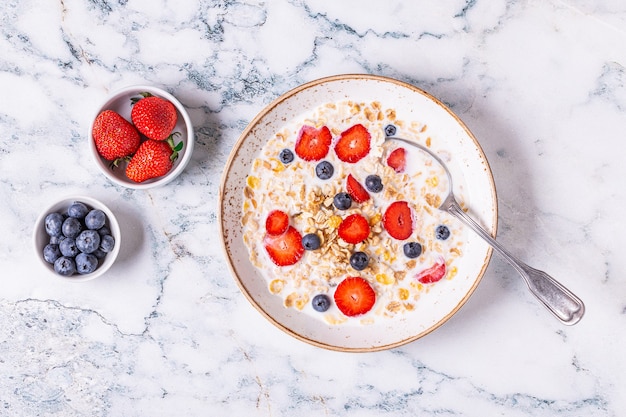 Healthy breakfast, bowl with oat granola, milk and berries, top view.