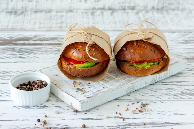 Здоровый завтрак - гамбургер с копченым лососем, листьями салата и авокадо подается в крафт-бумаге на деревянном фоне, горизонтально.