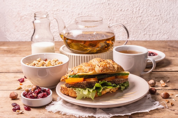 Healthy breakfast concept. Morning good mood with tea, croissant, granola, milk, and jam. Vintage wooden table, copy space