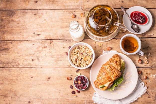 Healthy breakfast concept. Morning good mood with tea, croissant, granola, milk, and jam. Vintage wooden table, top view