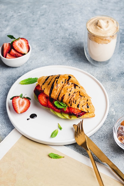 Sana colazione croissant sandwich con kiwi, fragole, menta, salsa al cioccolato e dalonga caffè e giornale. concetto di colazione francese. consegna del cibo. vista dall'alto con copyspace.