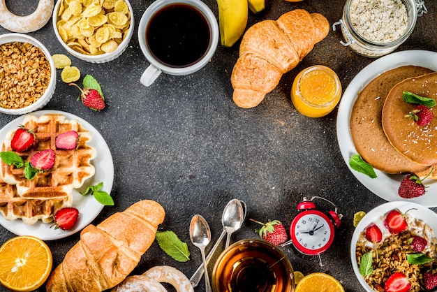 Фото Концепция здорового завтрака, разнообразная утренняя еда - блины, вафли, сэндвич с овсяной кашей и мюсли с йогуртом, фруктами, ягодами, кофе, чаем, апельсиновым соком