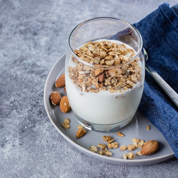 Healthy Breakfast Food. Yogurt with granola and nut in glass on gray plate on stone table background