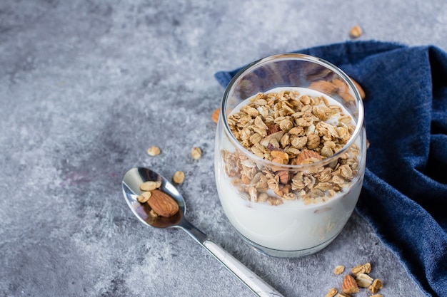 Healthy Breakfast Food. Yogurt with granola and nut in glass on gray plate on stone table background