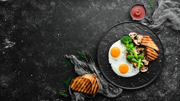 Healthy breakfast Fried egg with broccoli mushrooms and bread On a black stone plate Top view