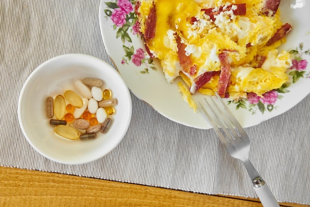 Healthy breakfast fried eggs with bacon in a plate and dietary supplements, vitamins and minerals on a wooden table