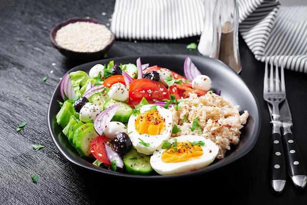 Healthy breakfast Greek inspired savory oatmeal with fresh cucumber tomatoes olives lettuce mozzarella cheese and boiled egg Top view