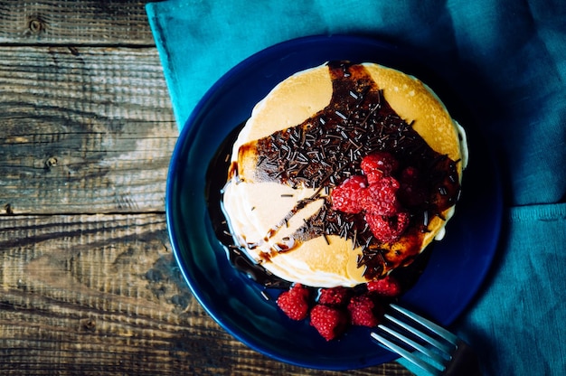 Healthy breakfast homemade pancakes with fresh raspberries and chocolate sauce on an old wooden table copy space