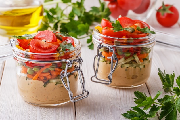 Healthy breakfast - hummus with vegetables in glass jars.