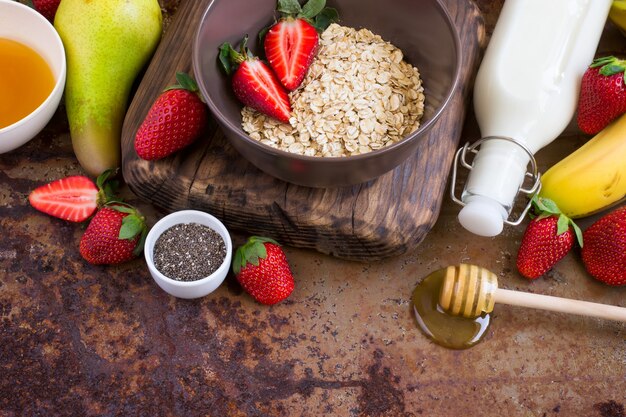 Ingredienti salutari per la colazione: farina d'avena, miele, frutta, fragola e semi di chia. concetto di cibo biologico naturale