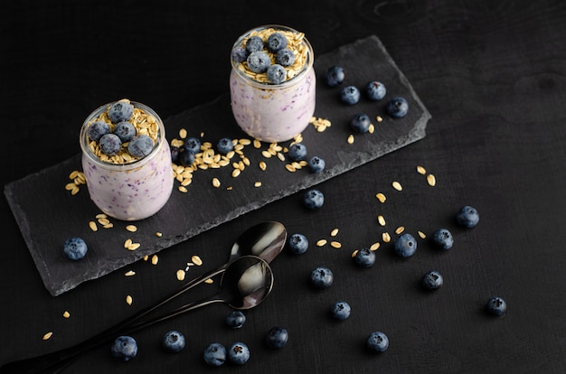 Healthy breakfast . Jars of homemade yogurt with blueberries and oats on black . Top view,copyspace