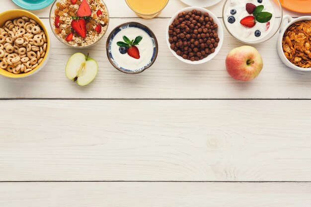 Healthy breakfast meals on wooden table copy space. Muesli, cornflakes, chocolate cereal balls and yogurt with berries frame, top view